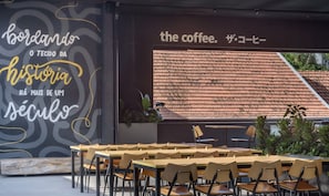Un espace extérieur aménagé avec des tables et des chaises en bois, un mur orné d’un texte et d’un motif décoratif, et une vue sur un toit recouvert de tuiles, visible à travers une fenêtre.