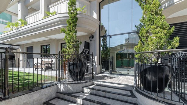 Une entrée moderne avec une façade en verre, un escalier en métal noir et un petit espace extérieur aménagé en coin salon.