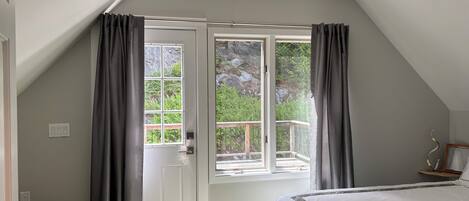 Camera da letto con un letto grande, una ventola a soffitto, una finestra con tende e vista su del verde all'esterno.