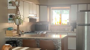 A modern kitchen with a central island, stainless steel appliances, and a dining area with wooden chairs and a table. - Cozy Vibe, Clean, Beach Access, 10 mins to GOTL! (Ashtabula)