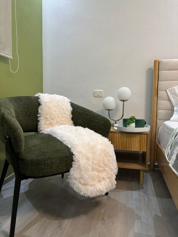 A room with a green armchair, a fluffy white throw, a bedside table with two lamps, and a bed with a wooden headboard. - Refuge in paradise (Dominicus)