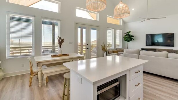 Una cocina moderna con una isla central, armarios blancos y una zona de comedor con mesa y sillas de madera.