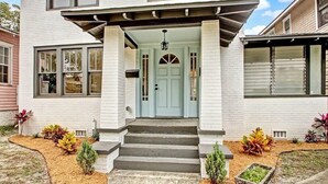 A two-story house with a light blue front door, white brick exterior, and a covered porch with steps leading to the entrance. - Springfield Charmer Clean, Spacious,  with WI-FI Close to all! (Jacksonville)