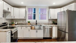 A modern kitchen with white cabinets, stainless steel appliances, a double sink, and a window with shutters. - Springfield Charmer Clean, Spacious,  with WI-FI Close to all! (Jacksonville)