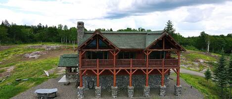Uma cabana de tronco com varanda, rodeada por uma área de cascalho e vegetação.