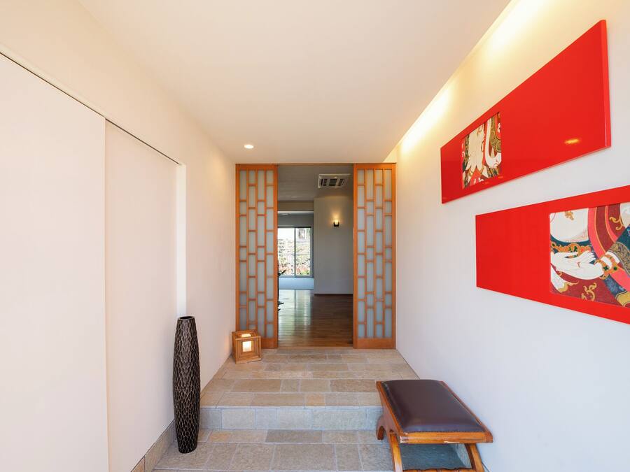 Un pasillo con un banco de madera, una pared decorativa con obras de arte rojas y un tradicional divisor japonés corredero.