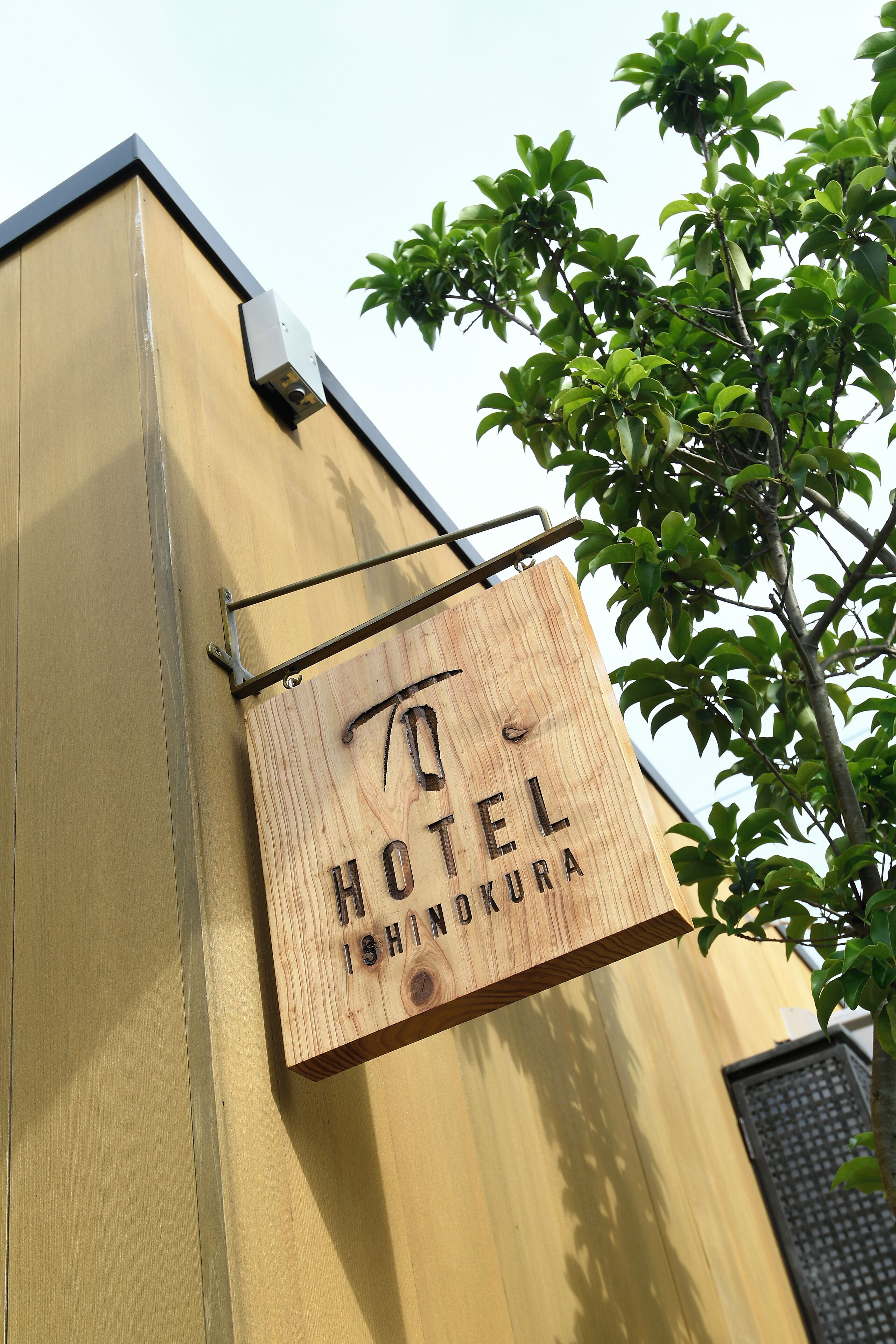 A wooden sign with "HOTEL ISHINOKURA" written on it, mounted on a building.