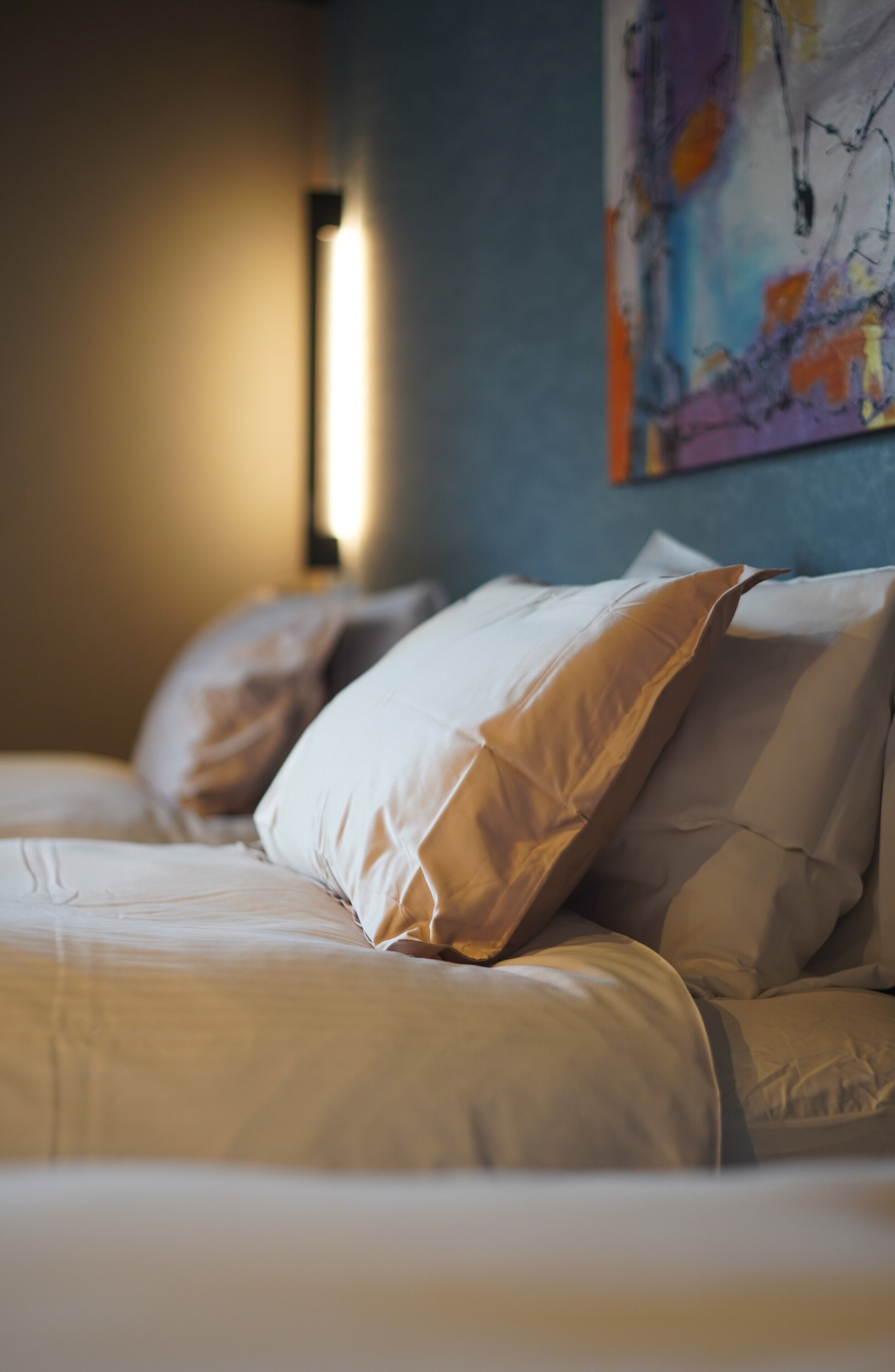 Un lit avec une literie blanche et un tableau abstrait aux couleurs vives accroché au mur.