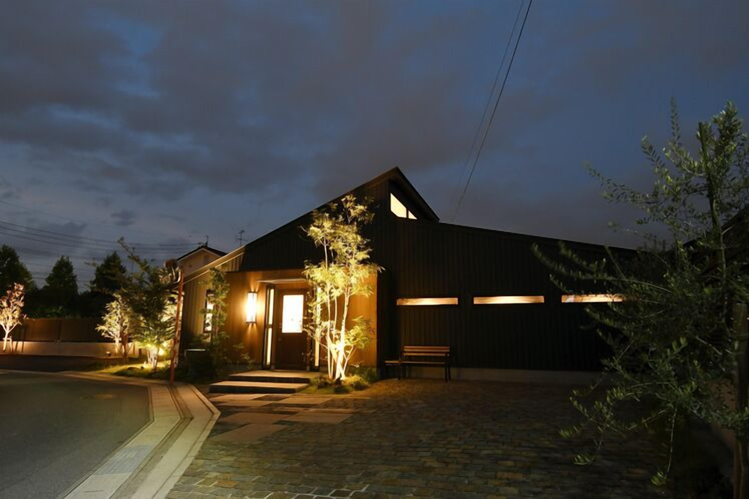 A building with a dark exterior, a lit entrance, and a paved driveway.