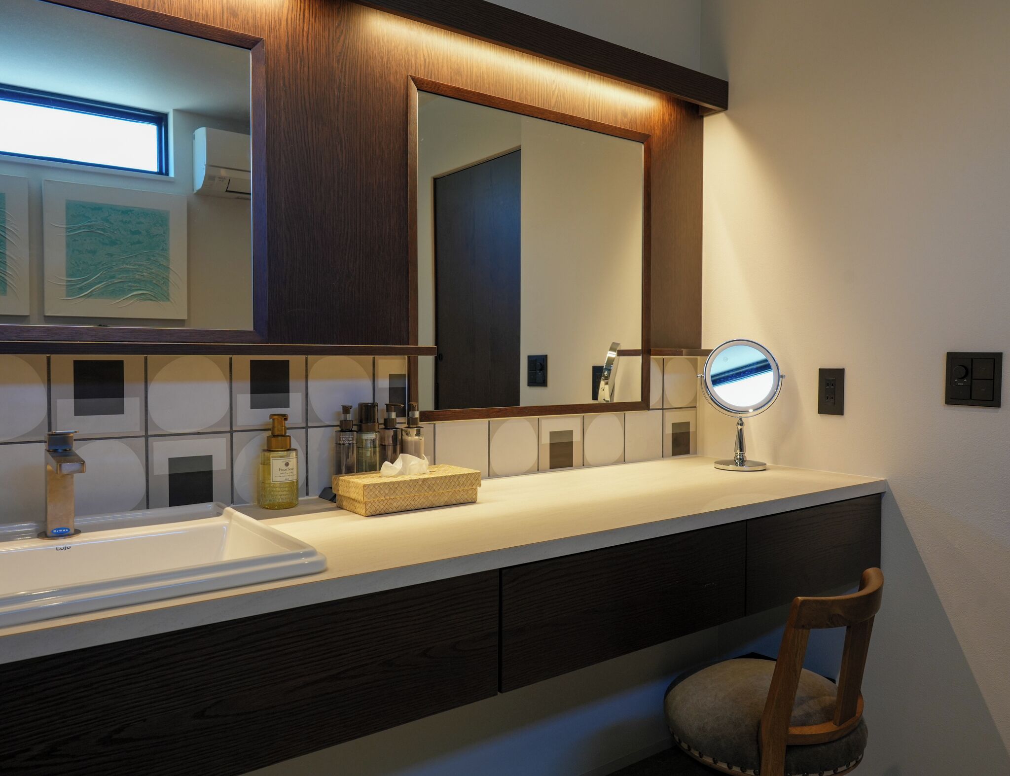 A modern bathroom with a large mirror, a sink, and a vanity with a chair.