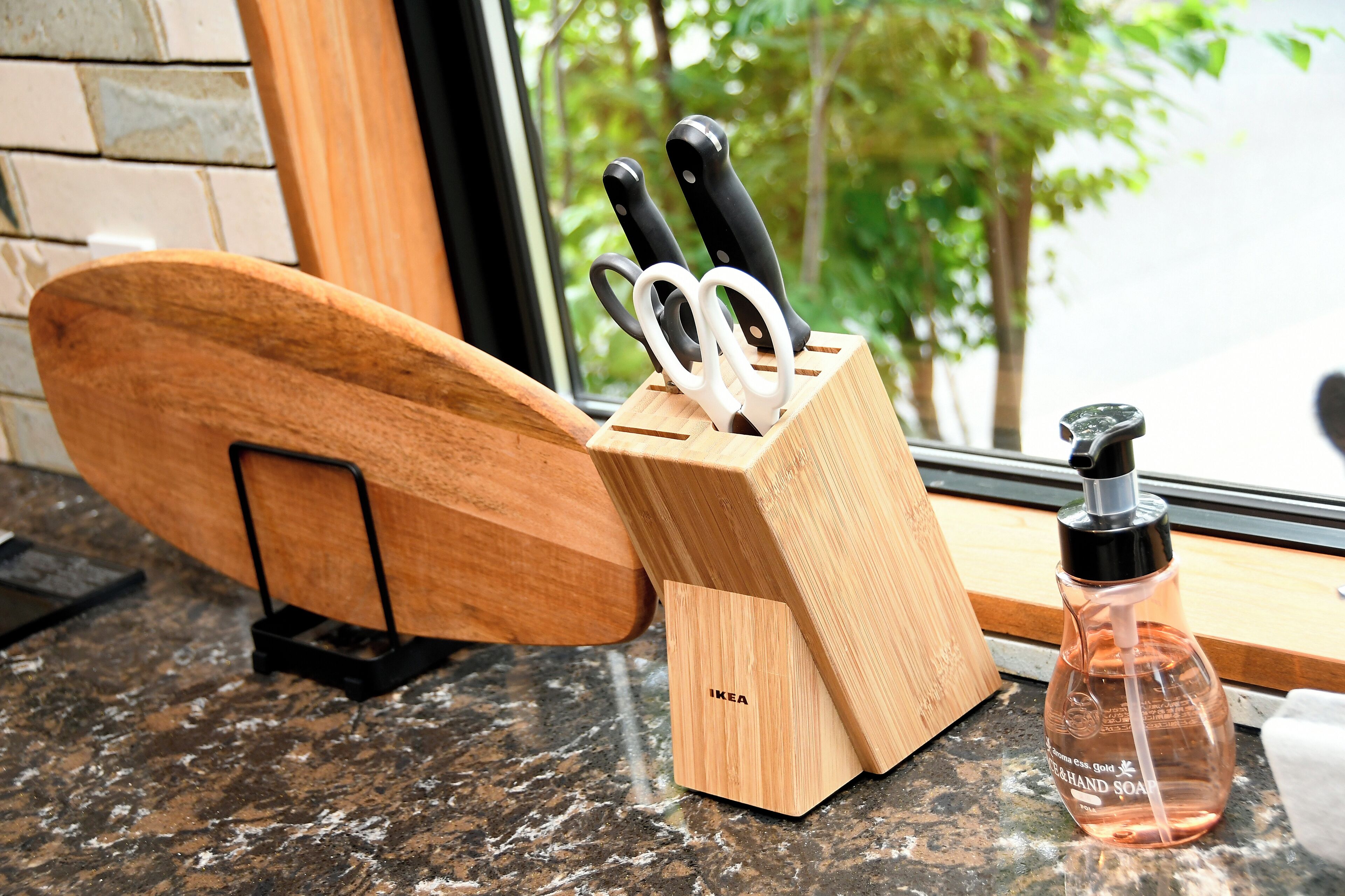 A kitchen counter with a wooden cutting board, a knife block with knives, and a bottle of soap.