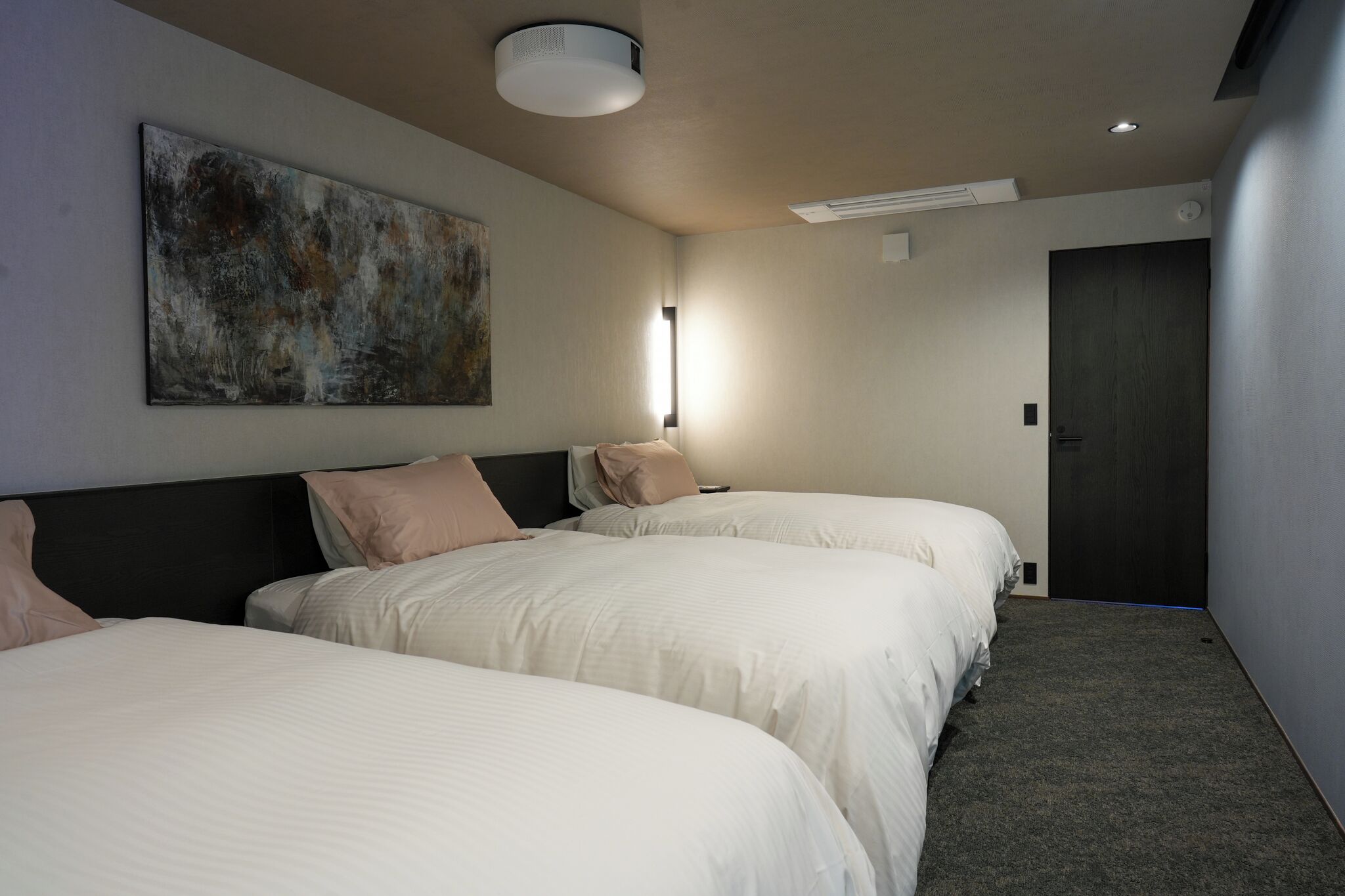 A hotel room with two beds, a large abstract painting on the wall, a ceiling light, and a door.