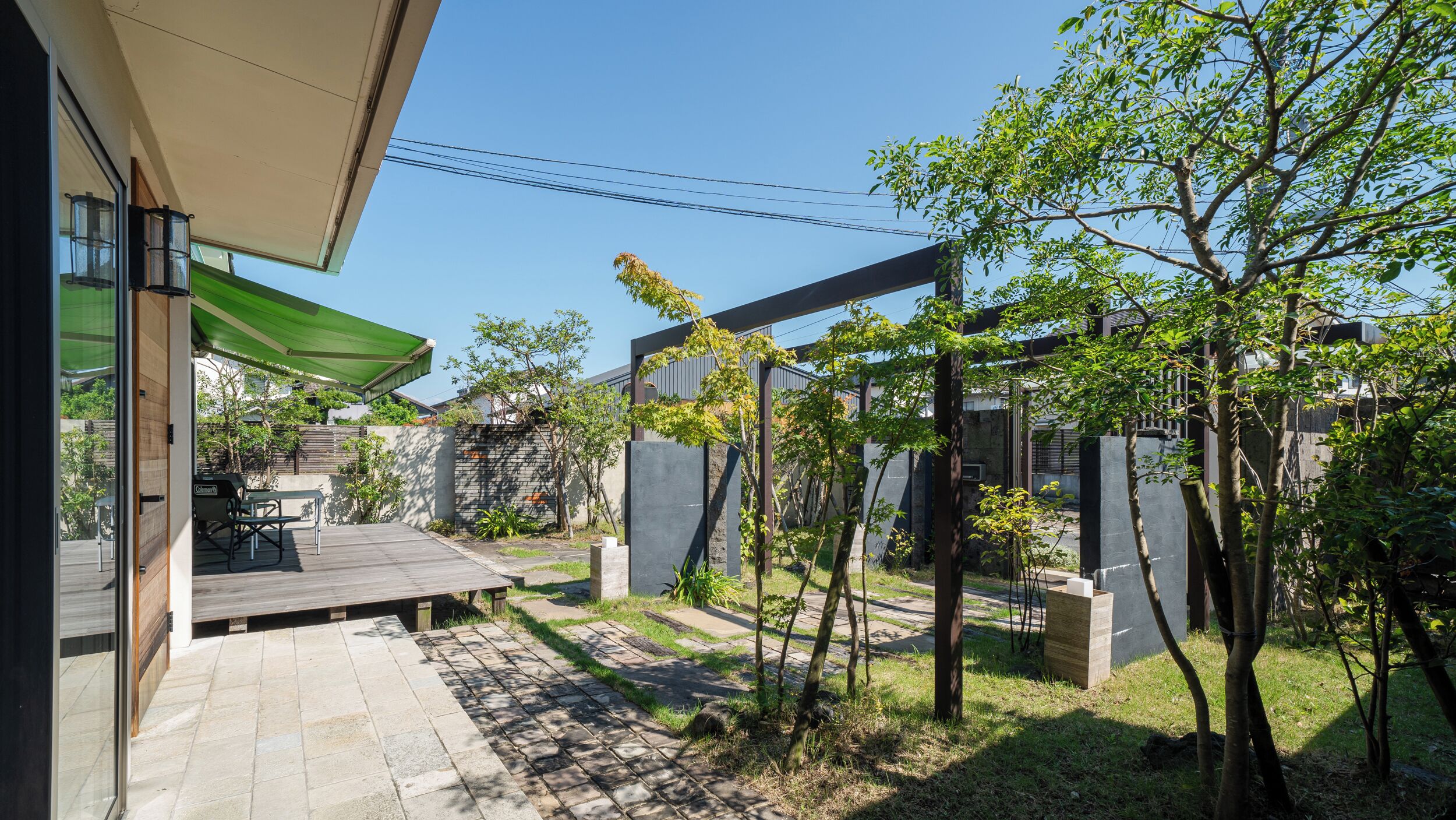 Un patio exterior moderno con terraza de madera, dosel verde y una parrilla.