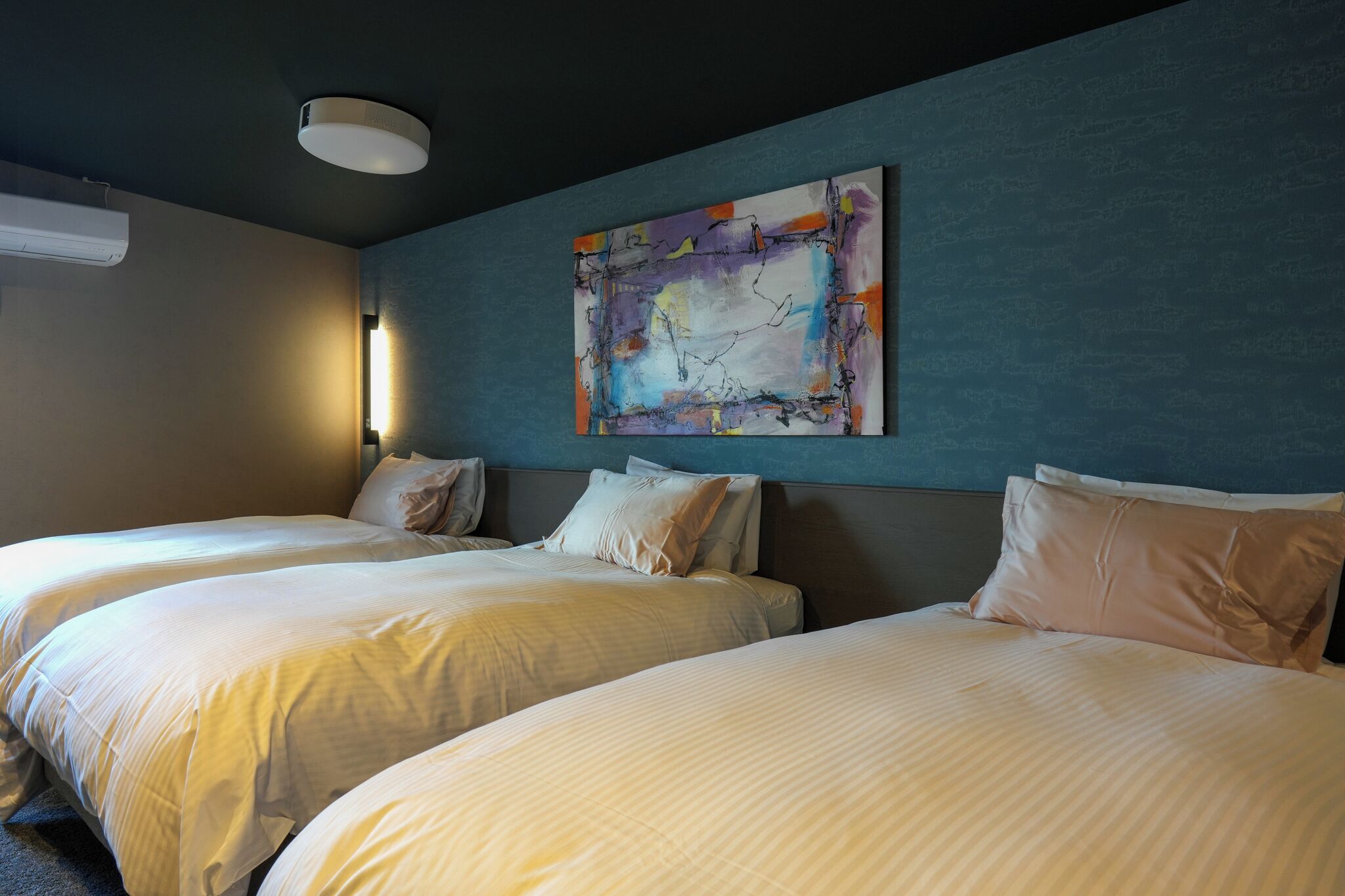 A hotel room with two beds, a large abstract painting on the wall, and a ceiling light fixture.