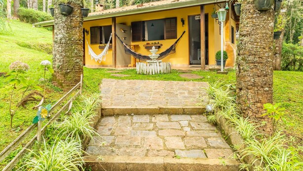 Una casa con una escalera de piedra que lleva a una puerta, rodeada de abundante vegetación y una hamaca.