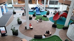 Un grand espace intérieur comprenant plusieurs aires de jeux, des coins salon et des plantes en pot.