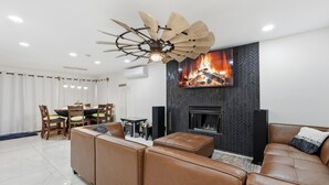 A modern living room with a fireplace, leather sofas, a dining area, and a ceiling fan. - Spacious 4-bedroom house with WiFi and AC in fantastic Chandler (Chandler)