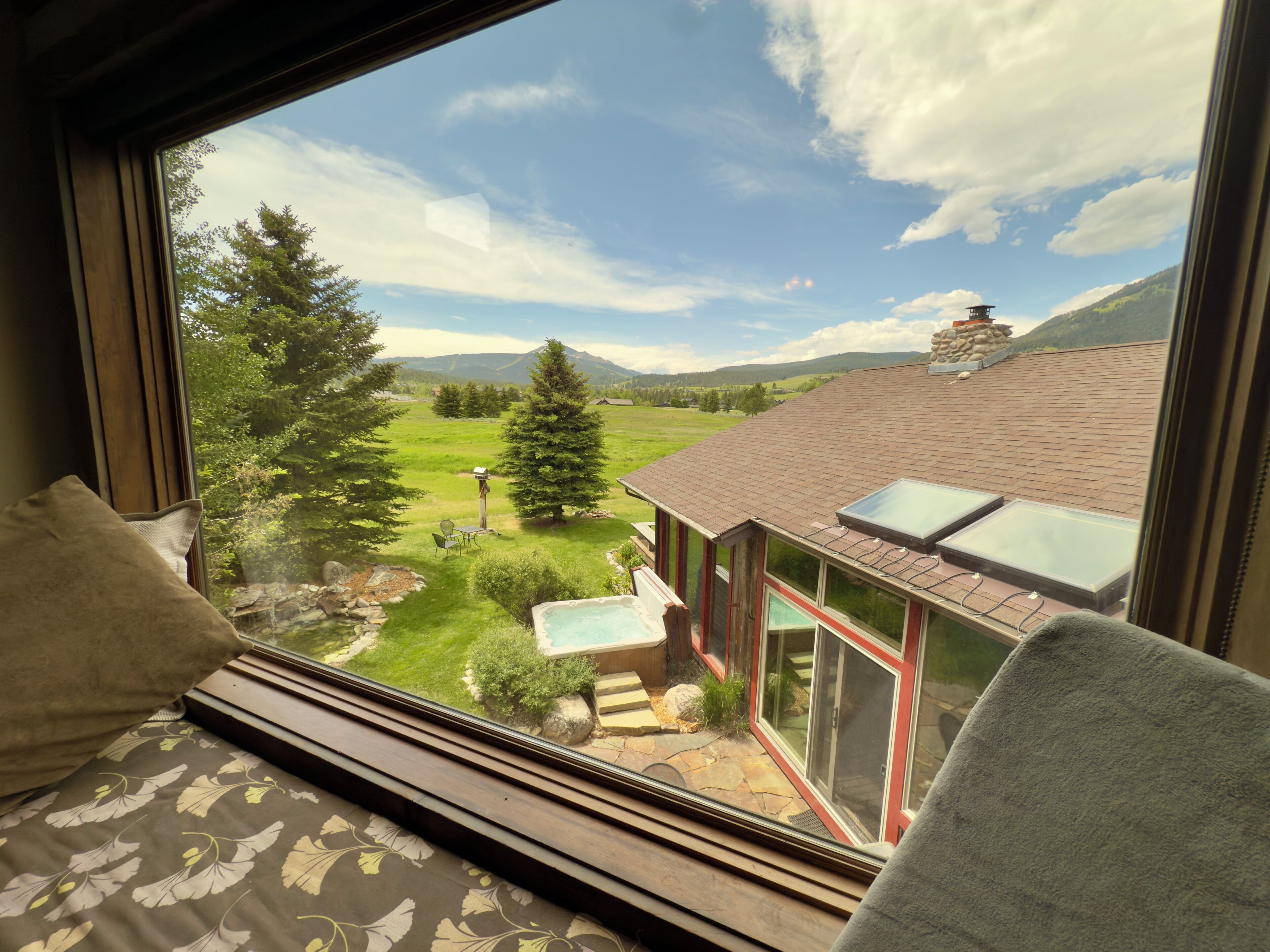 Habitación con una ventana grande que da a un jardín, una bañera de hidromasaje y vistas a la montaña.