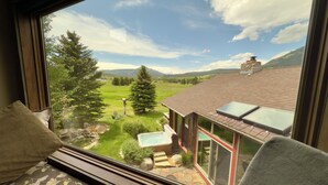 A room with a large window overlooking a garden, a hot tub, and a mountain view. - Spacious 4-bedroom house with private Sauna, Hot tub, Fitness room in Big Sky (Big Sky)