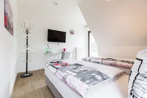 A modern bedroom with two beds, a flat-screen TV, a coat rack, and a desk with a chair.