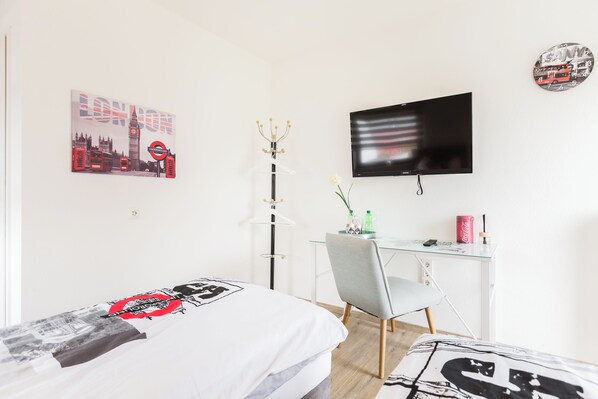 A bedroom with a bed, a desk, a chair, a TV, and a wall clock. - MY Messe & Business Home Refrath (Bergisch Gladbach)