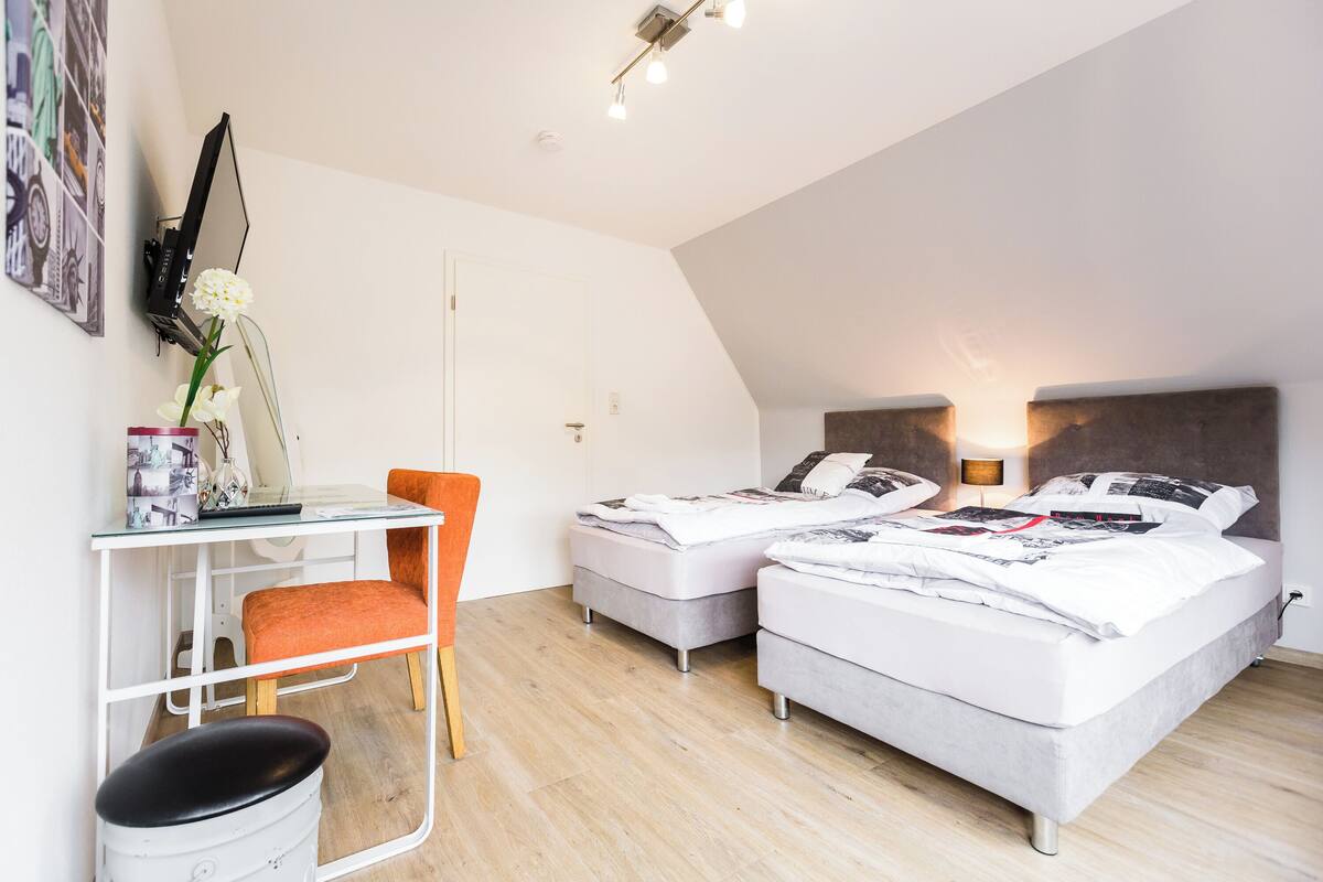 A modern bedroom with two beds, a desk, and a chair.