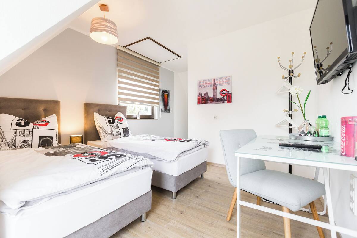 A modern bedroom with two beds, a desk, and a chair.