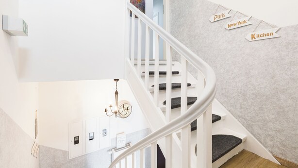 A modern staircase with a white railing, a chandelier, and a wall with tags labeled "Paris," "New York," and "Kitchen."