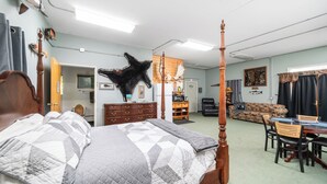 A bedroom with a four-poster bed, a wooden dresser, a dining table with chairs, a sofa, and a mounted animal hide. - Rustic Retreat Under the Stars - Quiet, Cozy, & Woodsy - high speed WIFI (Fairbanks)