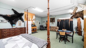 A room with a four-poster bed, a dining table with chairs, a sofa, a wooden cabinet, and a mounted moose head. - Rustic Retreat Under the Stars - Quiet, Cozy, & Woodsy - high speed WIFI (Fairbanks)