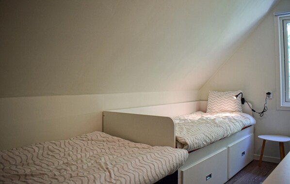 A small, single-room apartment with a sloped ceiling, a bed with a patterned bedspread, a bedside table, and a window with a view.