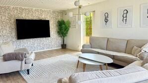 Un salon moderne doté d’un grand téléviseur à écran plat, d’un canapé beige, d’une table basse blanche et d’un tapis à motifs.