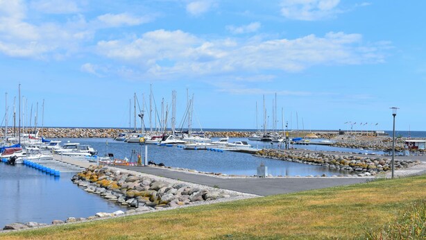 Un port de plaisance où sont amarrés de nombreux bateaux, une digue rocheuse et un ciel dégagé.