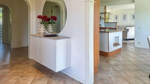 Un intérieur moderne avec un comptoir d’accueil blanc, un miroir et un vase rempli de fleurs rouges. On y trouve également un coin cuisine avec un plan de travail en bois et une chaise blanche.