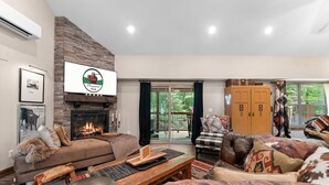A spacious living room with a fireplace, leather sofas, and a large window overlooking a balcony. - Ultimate Couples Escape w/ Hot Tub & Firepit + Free Family Tickets (Hollister)