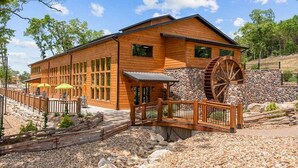 A wooden lodge with a large water wheel, outdoor seating, and a stone wall. - Ultimate Couples Escape w/ Hot Tub & Firepit + Free Family Tickets (Hollister)