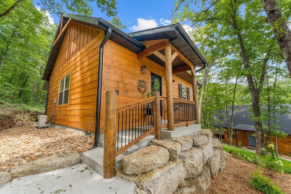 A wooden cabin with a porch, stone steps, and a stone wall.
