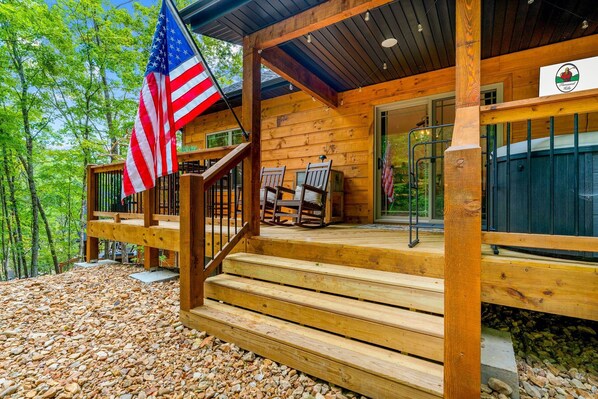 A wooden cabin with a porch, two rocking chairs, and an American flag.