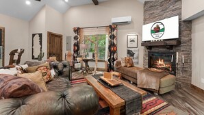 A cozy living room with a fireplace, a sofa, a coffee table, and a large window with curtains. - Ultimate Couples Escape w/ Hot Tub & Firepit + Free Family Tickets (Hollister)
