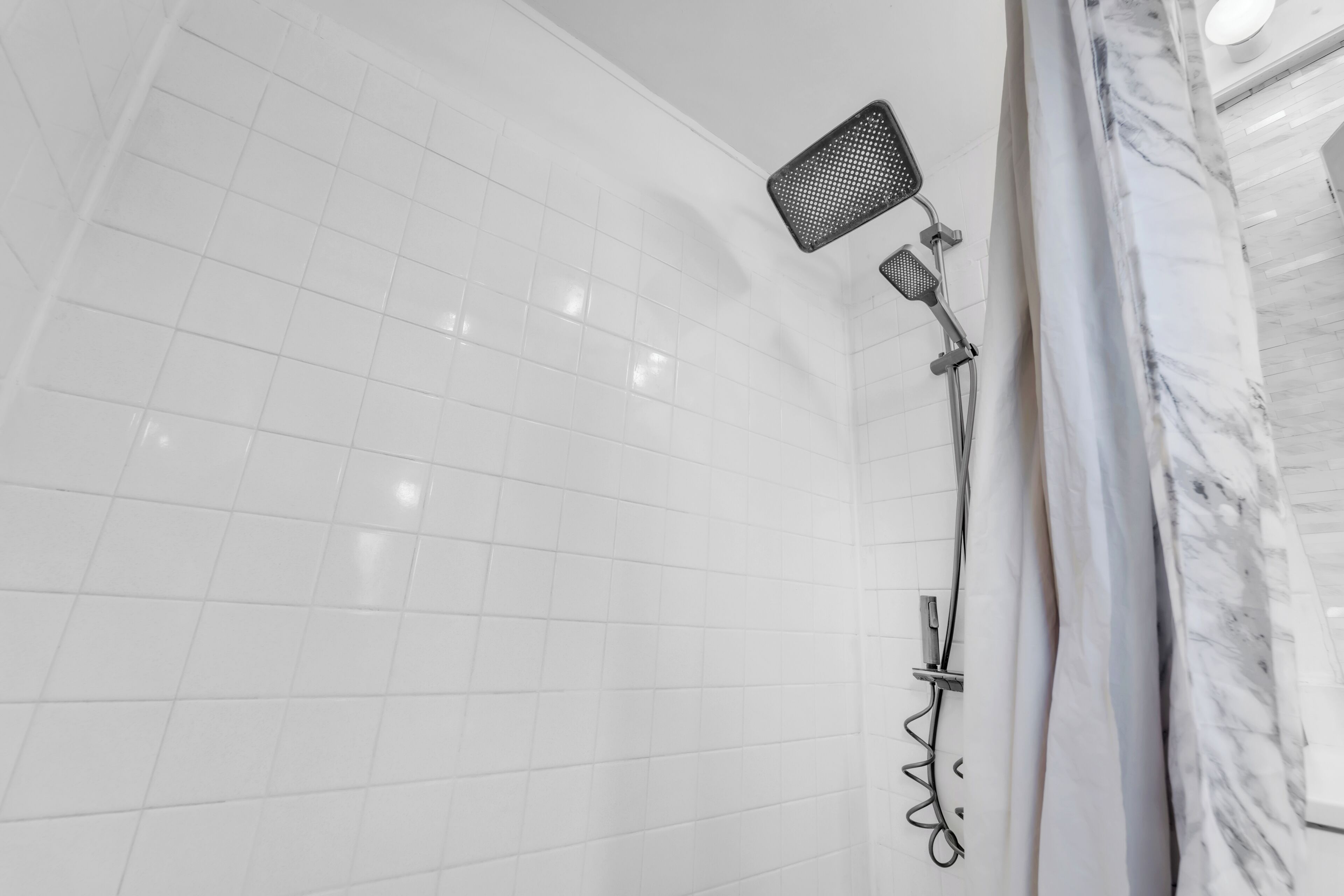 A bathroom with white tiled walls, a shower with a handheld showerhead, and a marble accent wall.