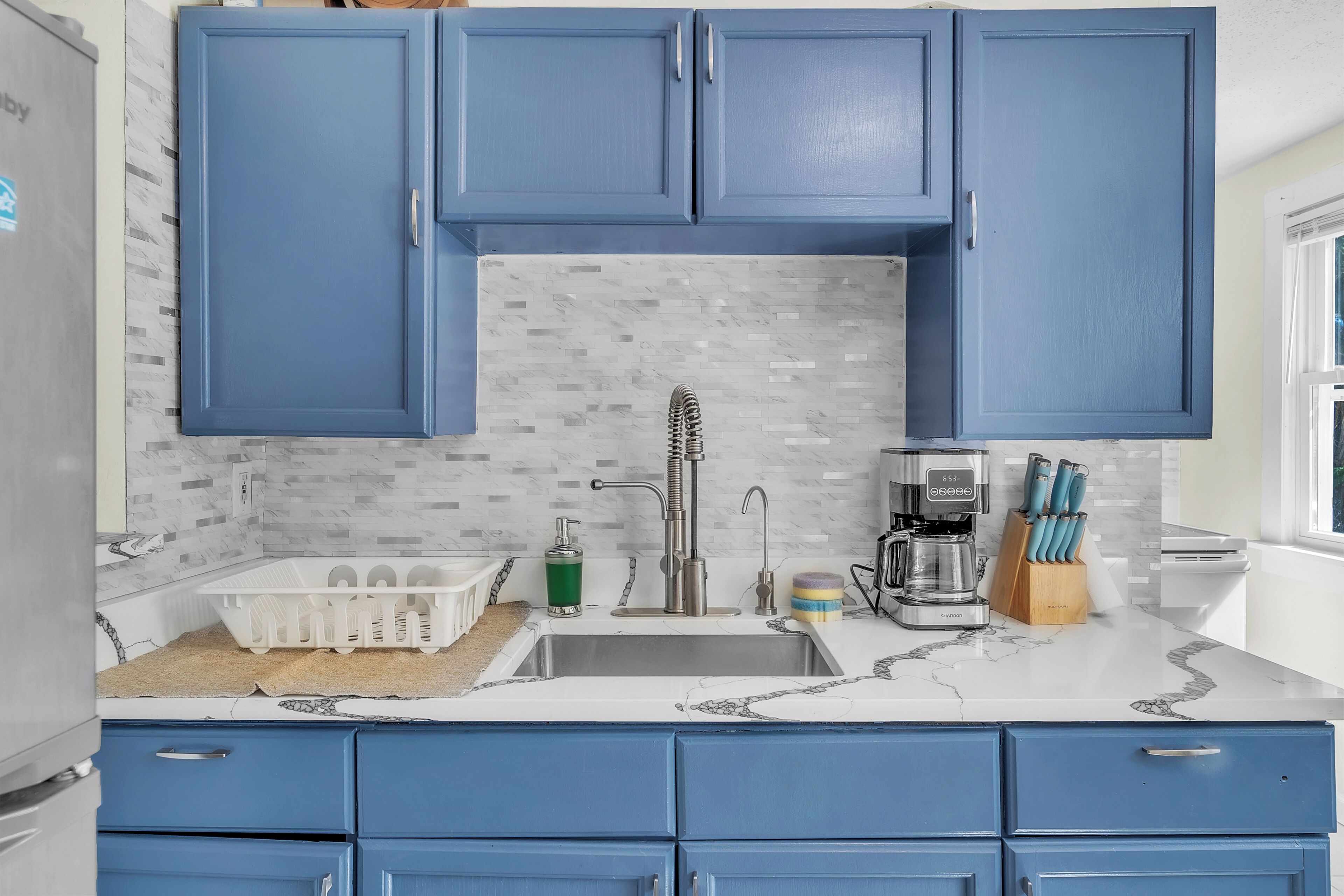 A kitchen with blue cabinets, a marble countertop, and a coffee maker.