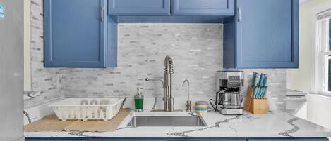 A kitchen with blue cabinets, a marble countertop, and a coffee maker.