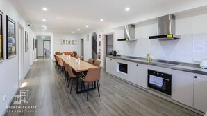 Una cucina moderna con un lungo tavolo da pranzo, mobili bianchi ed elettrodomestici in acciaio inossidabile.