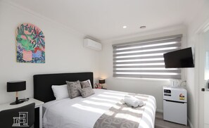 Ein modernes Hotelzimmer mit Bett, Nachttischen, einem Flachbildfernseher, einer Klimaanlage und einem Fenster mit Jalousien.