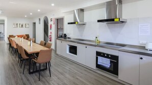 A modern kitchen with a long dining table and chairs, a built-in oven, and a stainless steel range hood.