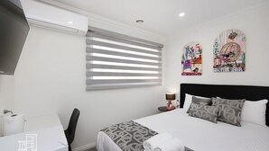 A hotel room with a bed, a desk, and a window with blinds.