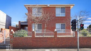 A two-story brick building with a white fence, a tree in front, and a traffic light.