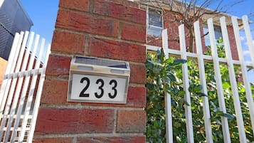 A brick wall with a house number sign '233' and a white picket fence.