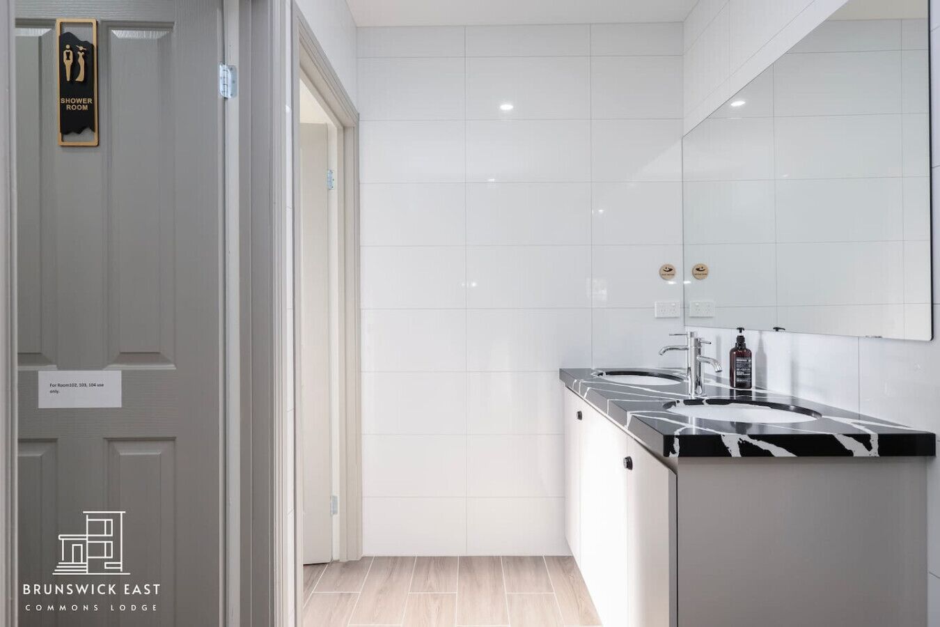 Une salle de bain moderne avec un grand miroir, un lavabo sur un plan de toilette noir et un panneau indiquant l’emplacement de la douche.
