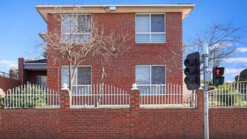 A two-story brick building with a white picket fence, a tree in front, and a traffic light.
